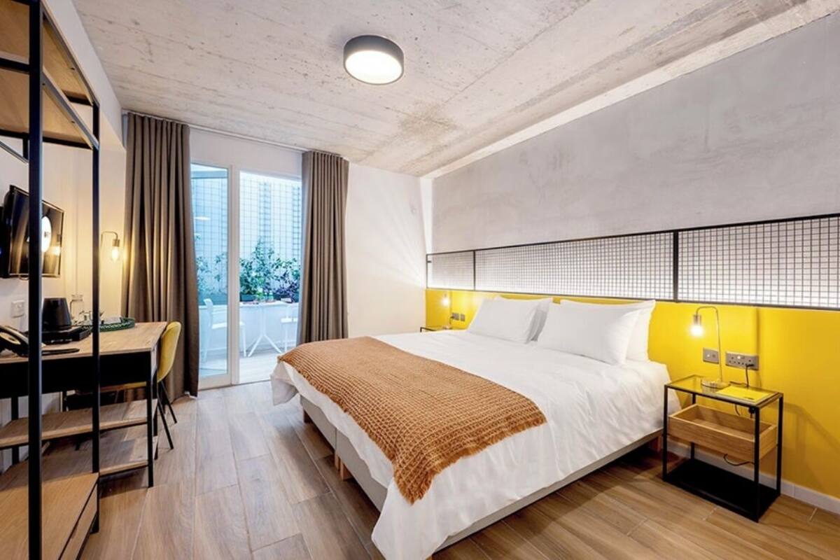 Ein modernes Hotelzimmer mit einem großen Bett, einem Schreibtisch mit Stuhl, einem Fernseher und einem Balkon mit Vorhängen.