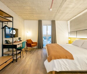 A hotel room with a bed, a desk with a computer, a chair, and a window with curtains. - Fort40 Guesthouse (Sliema)