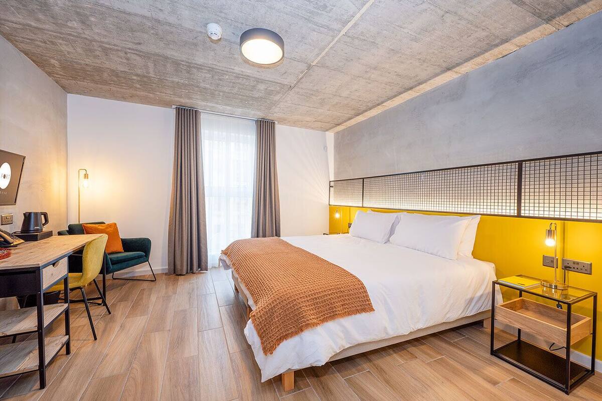 Ein Hotelzimmer mit einem großen Bett, einem Schreibtisch mit Stuhl, einer Kaffeemaschine und Blick ins Freie.