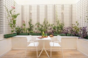 A small patio with a table and chairs, surrounded by a variety of potted plants and climbing vines against a tiled wall. - Fort40 Guesthouse (Sliema)