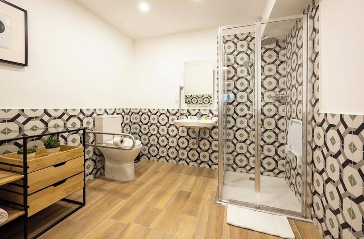 Un baño con ducha, inodoro, lavabo y una estantería de madera.