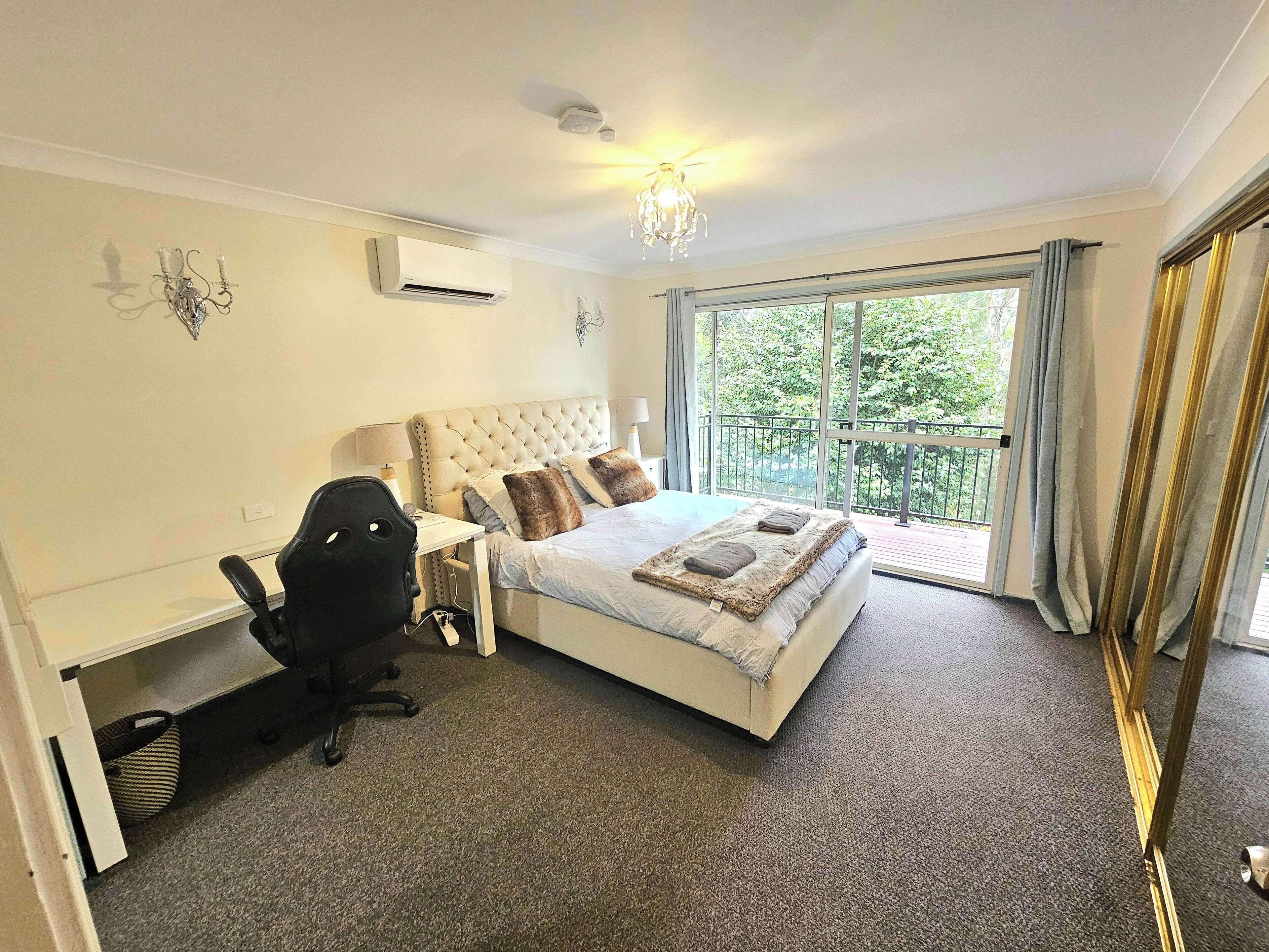 A bedroom with a large bed, a desk, a chair, and a balcony with curtains.
