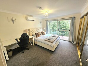 A bedroom with a large bed, a desk, a chair, and a balcony with curtains. - Luxury Mountain Retreat, 6 Bedroom, 3 Bathroom with Gym and Heated Swimming Pool (Springwood)