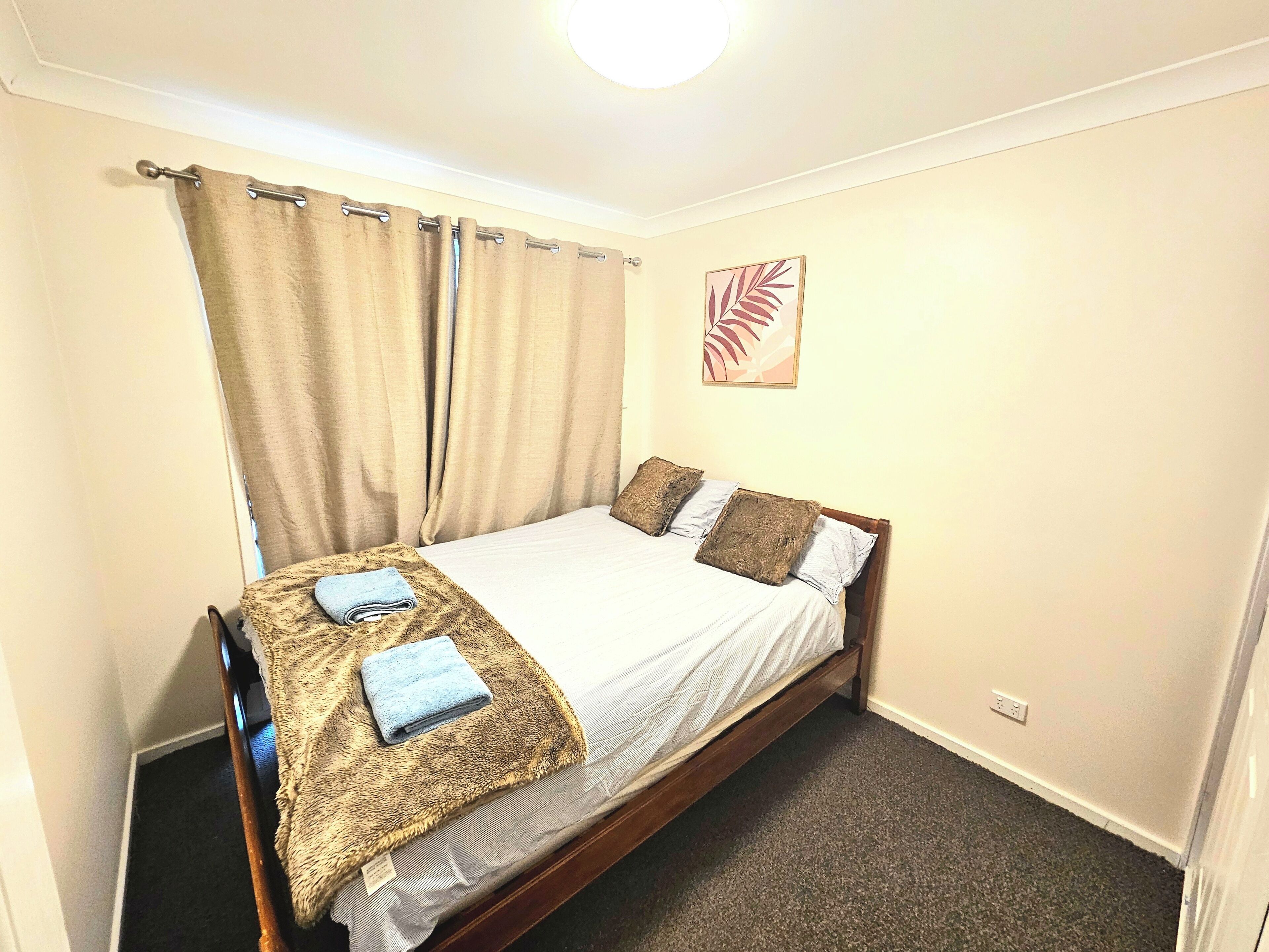 A small, neatly made bed with a white sheet and two pillows, a brown throw blanket, and a folded towel on the side.