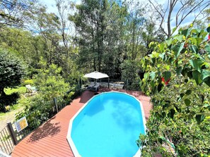 A swimming pool with a wooden deck, surrounded by lush greenery and trees. - Luxury Mountain Retreat, 6 Bedroom, 3 Bathroom with Gym and Heated Swimming Pool (Springwood)