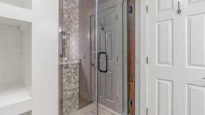 Una ducha con cerramiento de vidrio, pared con azulejos, una puerta blanca con manija y un marco blanco.