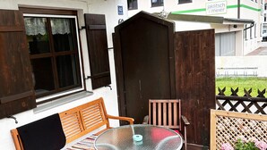 Eine Terrasse im Freien mit einem Glastisch, Holzstühlen, einer Bank und einem Blumentopf.