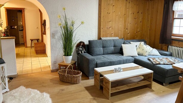 Ein gemütliches Wohnzimmer mit einem grauen Sofa, einem weißen Couchtisch und einem Holzboden.