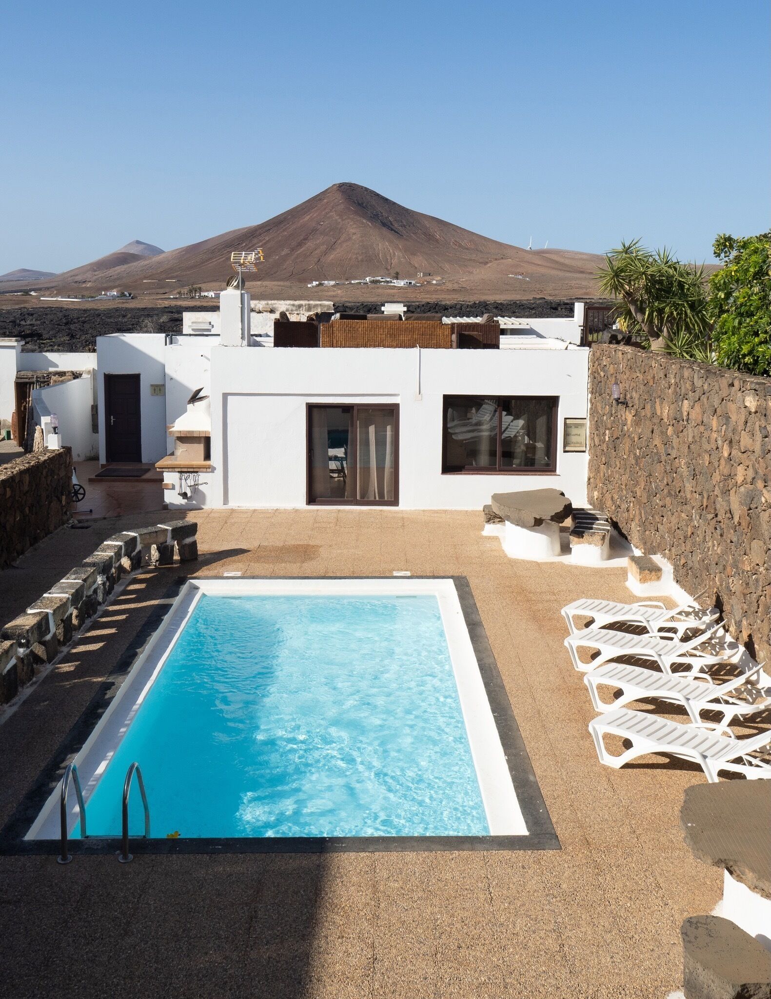 A pool with a clear blue water surface, surrounded by a sandy area with white lounge chairs.