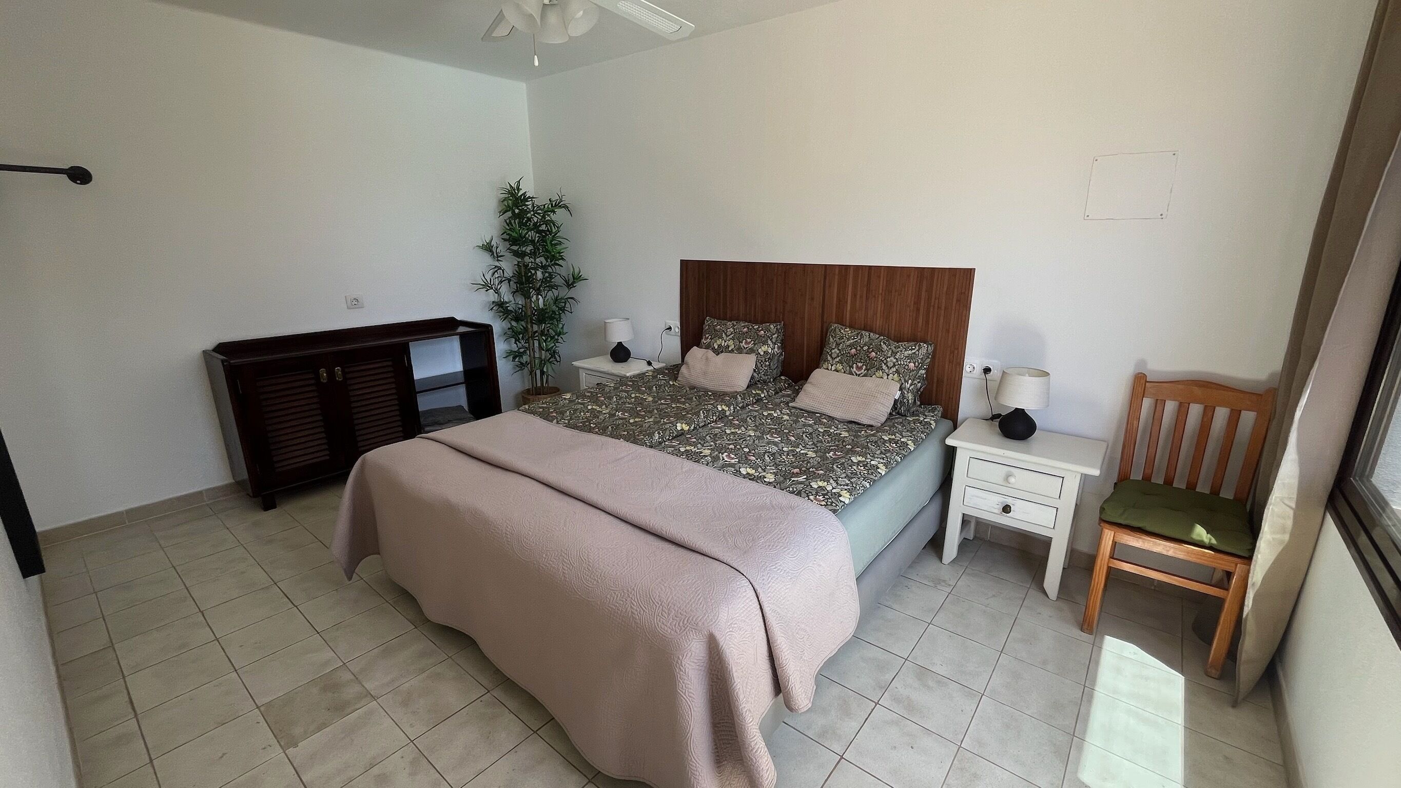 A bedroom with a bed, bedside tables, a chair, a plant, and a wardrobe.