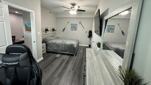 A bedroom with a bed, a desk, a chair, a ceiling fan, and a large mirror.