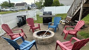A patio with Adirondack chairs, a fire pit, and a grill.