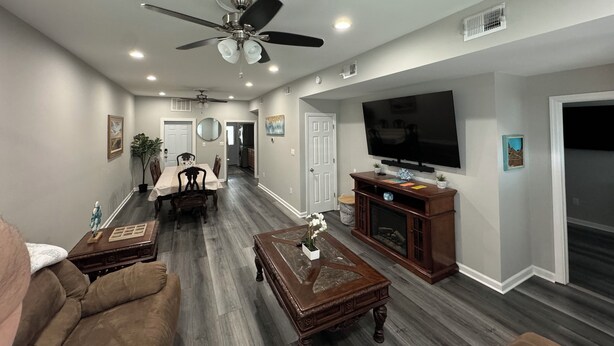 A spacious living room with a ceiling fan, a TV mounted on the wall, and a dining area with a table and chairs.