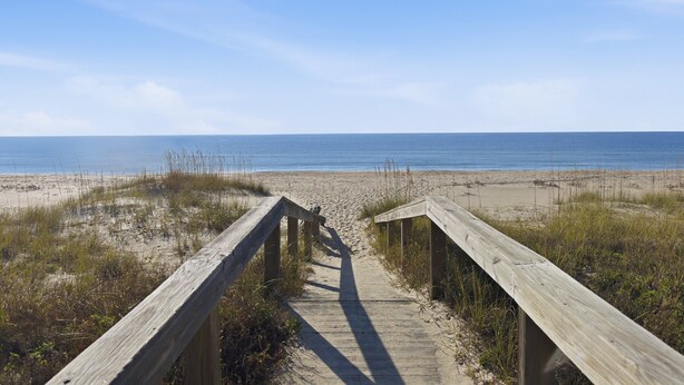 Une promenade en bois qui mène à une plage offrant une vue dégagée sur l’océan.
