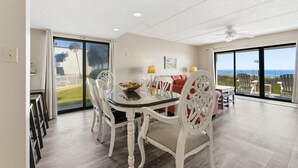 Un espace repas comprenant une table et des chaises, un canapé et une vue sur l’océan grâce à de grandes fenêtres.