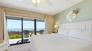 Une chambre avec un grand lit, une vue sur l’océan, un ventilateur de plafond et une table de chevet avec une lampe.