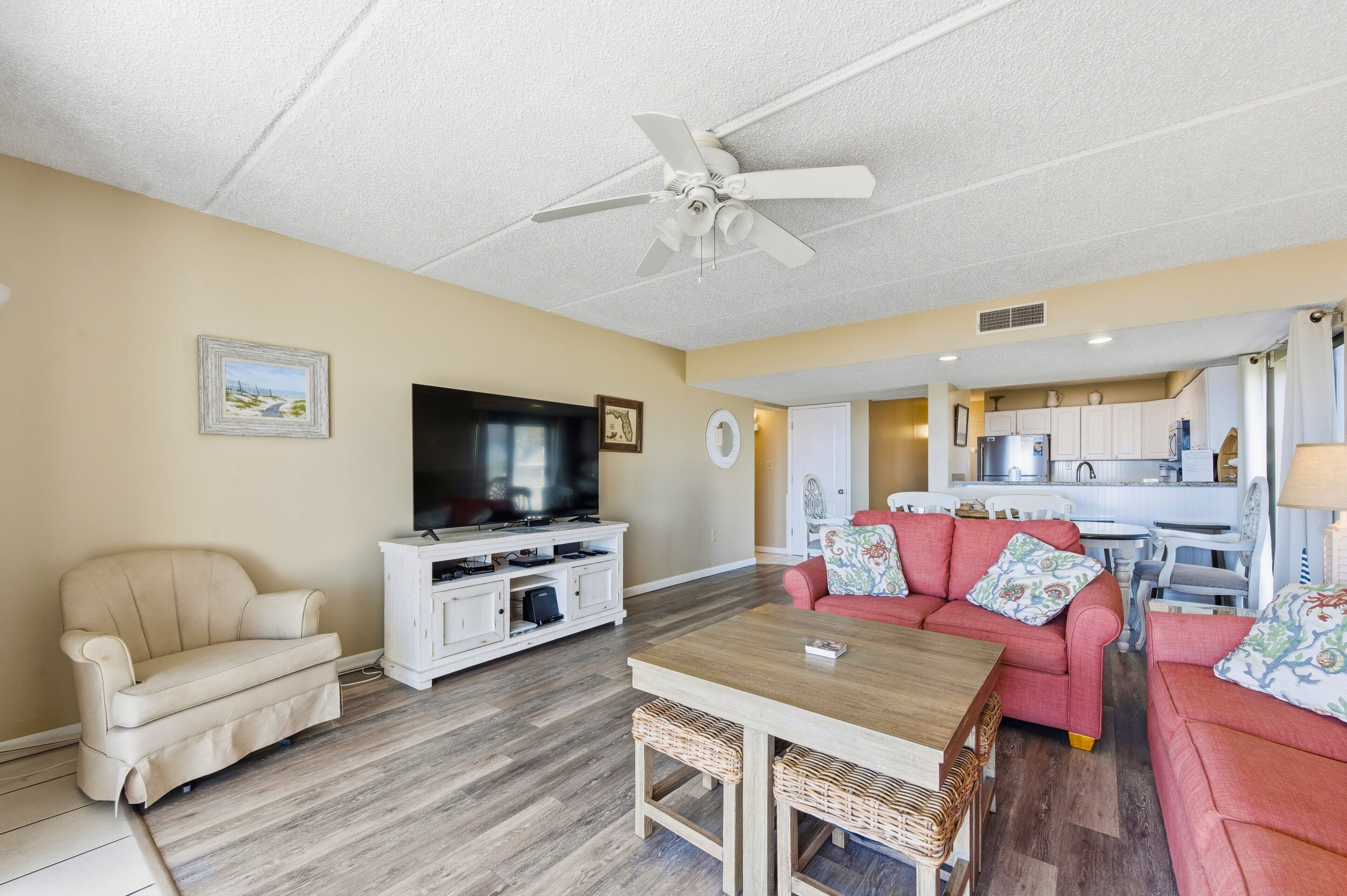 A living room with a beige sofa, a red sofa, a wooden table, a TV, and a ceiling fan.