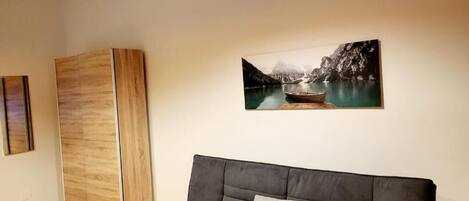 A modern living room with a grey sofa, a wooden cabinet, and a framed landscape painting on the wall.