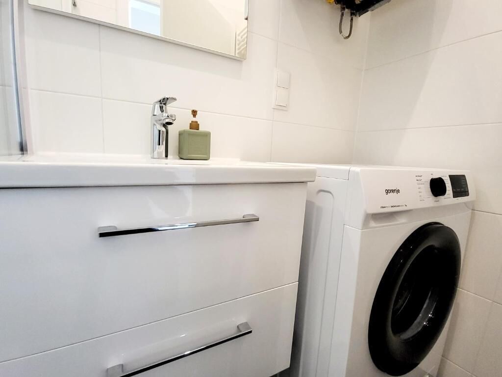 A modern bathroom with a white sink, a mirror, and a front-loading washing machine.