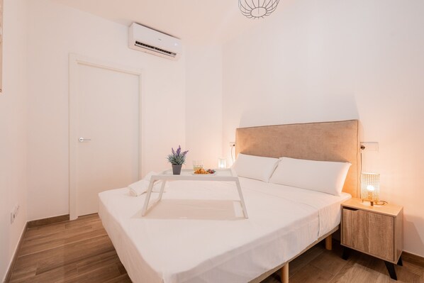 A neatly made bed with a wooden headboard, a bedside table with a lamp, and a small potted plant on the nightstand.