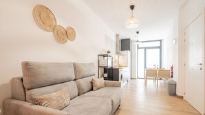 Un salon moderne avec un canapé beige, un coin repas avec une table et des chaises, et une cuisine en arrière-plan.