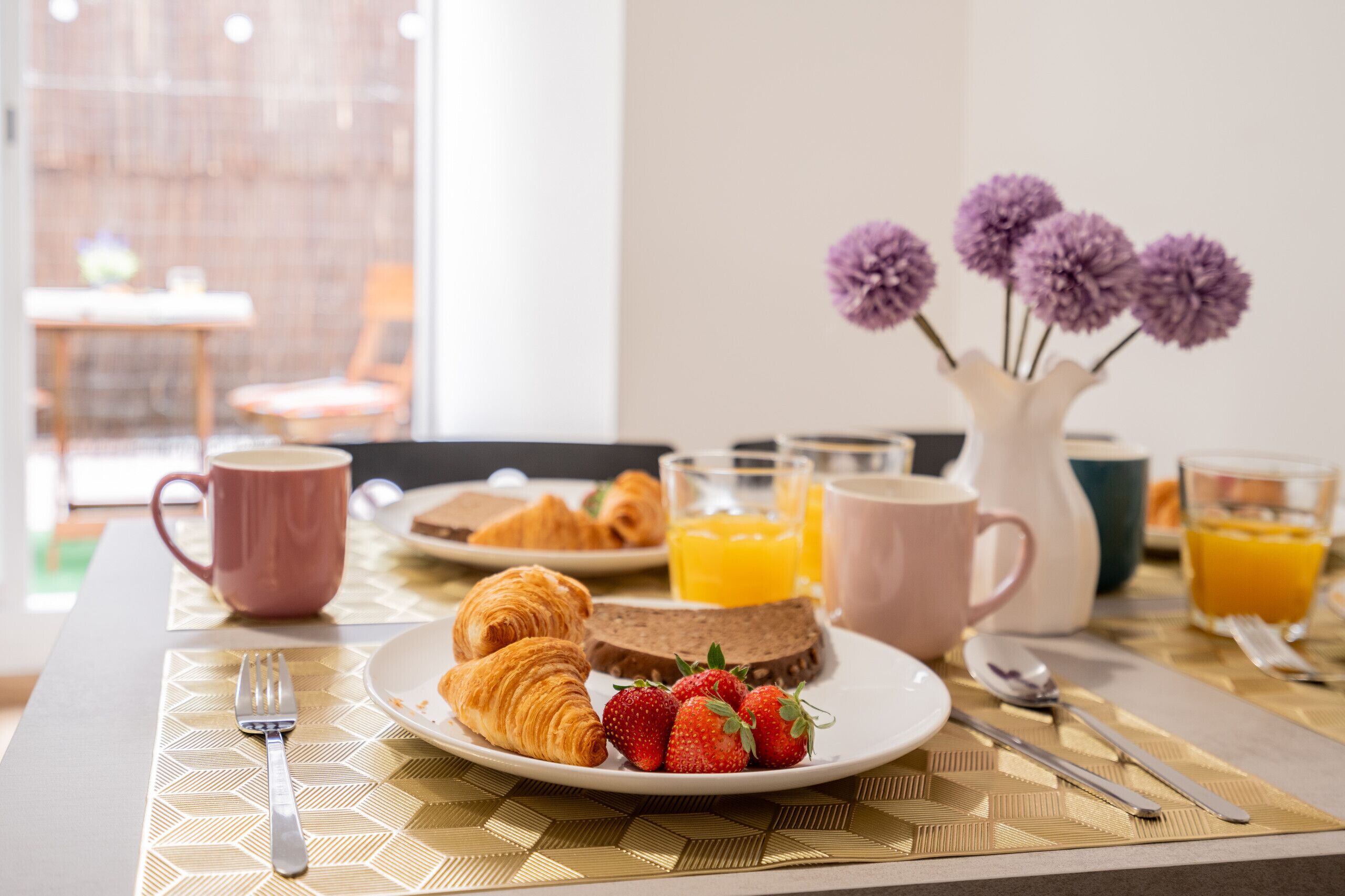 Una mesa de desayuno con cruasanes, fresas y jugo.