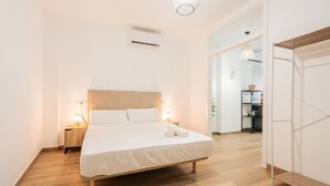 Een moderne hotelkamer met een houten vloer, een groot bed met witte lakens, nachtlampjes en een ingebouwde airconditioning.