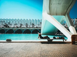 Ein Poolbereich mit einer modernen Architektur im Hintergrund, einem gefliesten Weg und einigen entspannten Personen am Pool.