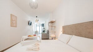 A modern hotel room with a large bed, a bedside table with a fruit bowl, a TV mounted on the wall, and a walk-in closet with shelves.