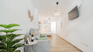 A modern living room with a grey sofa, a small round table with a bottle and glasses, and a large potted plant.