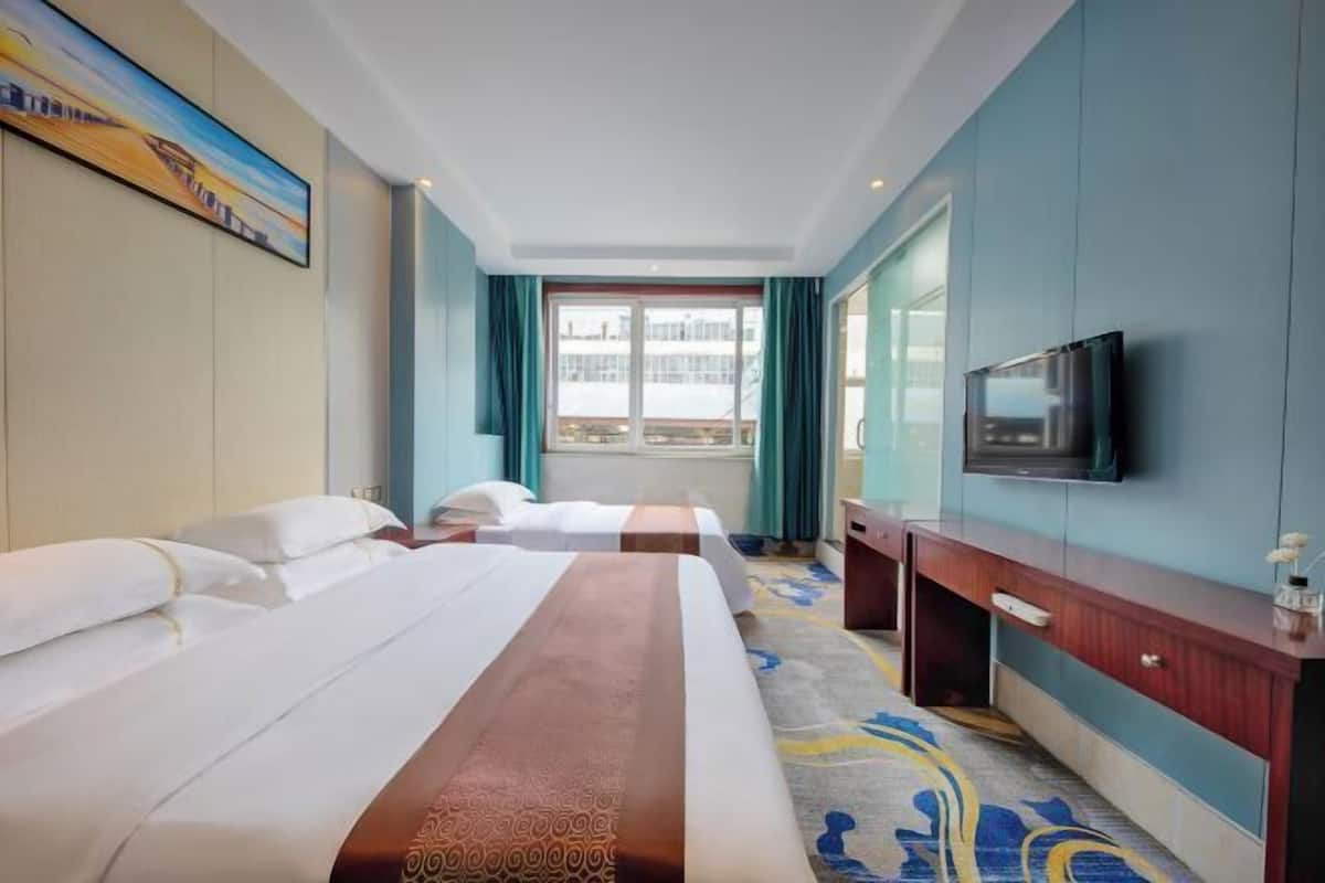 A hotel room with a large bed, a TV, a desk, and a window with curtains.