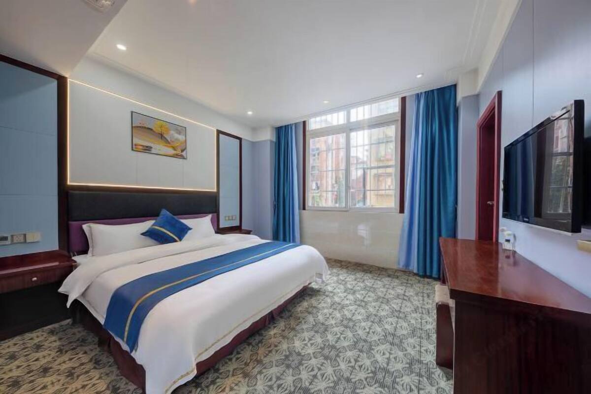 A hotel room with a large bed, a desk, a television, and a window with curtains.
