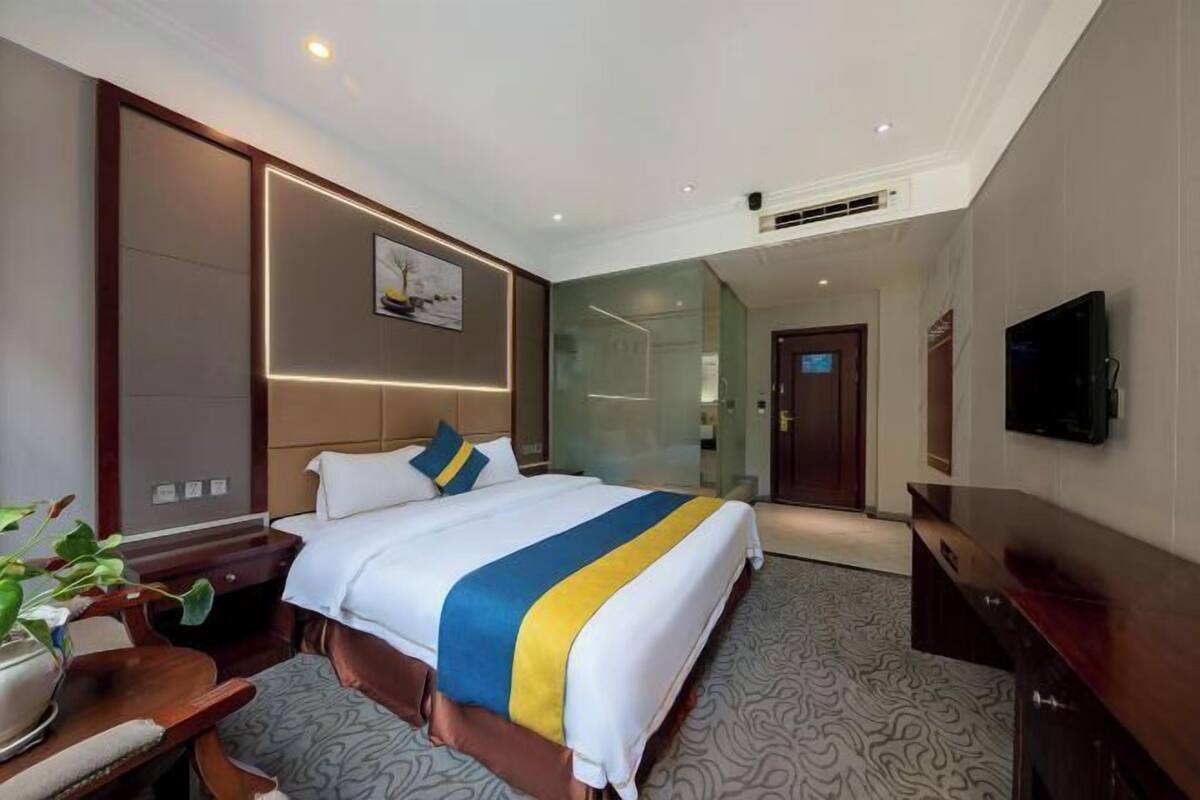A hotel room with a large bed, a desk, a chair, a television, and a plant.