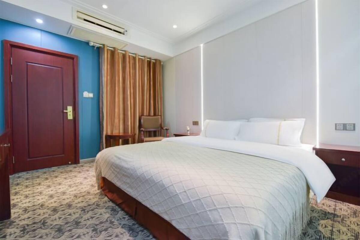 A hotel room with a large bed, a wooden nightstand, a desk, a chair, a wardrobe, and a curtain.
