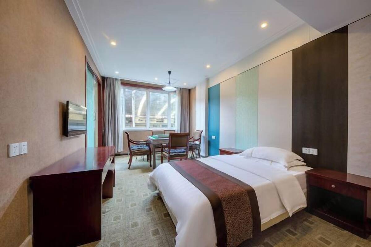 A hotel room with a bed, a desk, a chair, a TV, and a window with curtains.