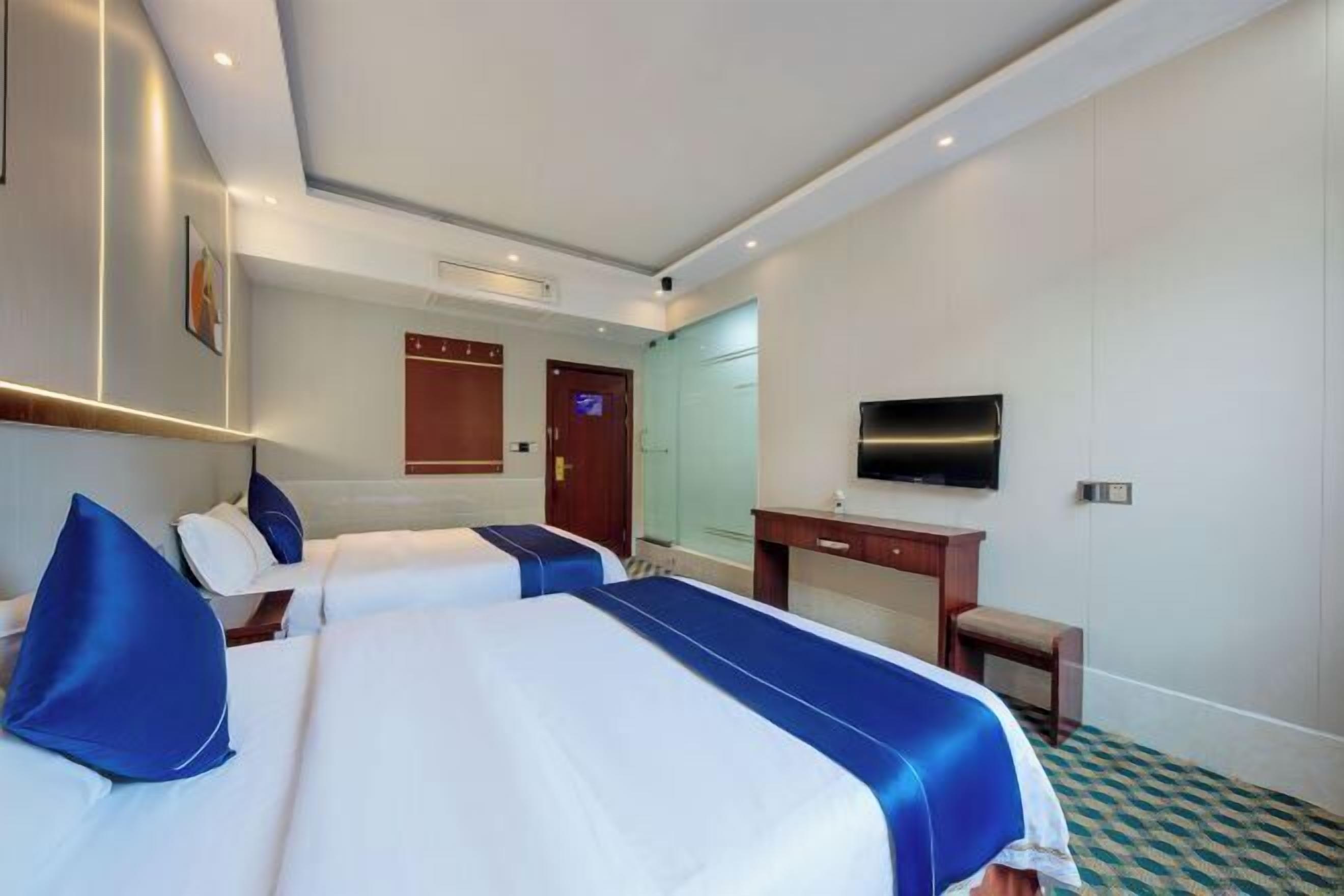 A hotel room with two beds, a desk, a TV, and a bathroom door.