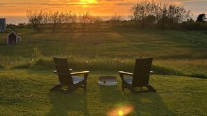 Two chairs facing a sunset over a grassy field with a small shed in the background.