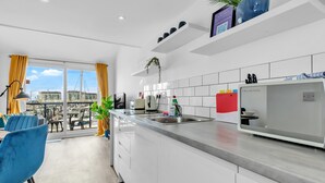 A modern kitchen with a built-in refrigerator, a sink, and a dining area with blue chairs. - On the Water 5 A One-of-a-Kind Stay | Free Parking | By My Getaways (Brighton)