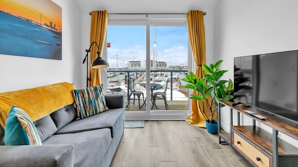 A modern living room with a sofa, TV, and a balcony with a view of boats and buildings. - On the Water 5 A One-of-a-Kind Stay | Free Parking | By My Getaways (Brighton)
