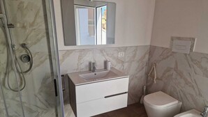 Un baño con cabina de ducha de vidrio, un lavabo blanco con encimera de mármol, inodoro y bidé.