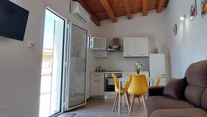 Un espacio habitable compacto con kitchenette, un comedor con sillas amarillas y un sofá marrón.