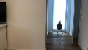 A spacious room with hardwood flooring, a bed, a television on a stand, and a large window with blinds.