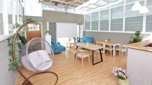 A modern interior with a wooden floor, a round table with chairs, a hanging chair, and large windows. - Xiaodou B&B (Taitung)