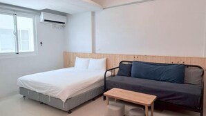 A bedroom with a bed, a sofa, a small table, and an air conditioning unit. - Xiaodou B&B (Taitung)