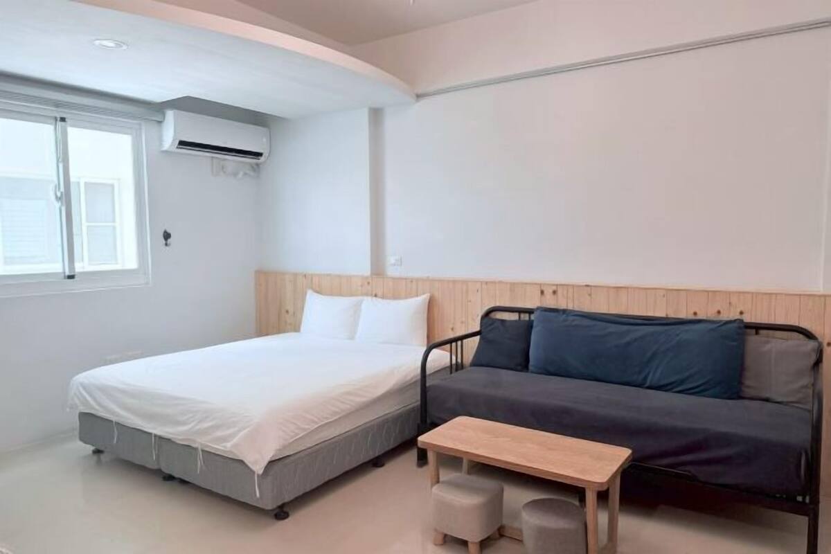 Un dormitorio con una cama, un sofá, una mesita y un equipo de aire acondicionado.