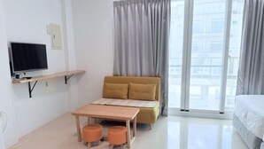 A modern hotel room with a sofa, a small table, a TV, and a balcony with curtains. - Xiaodou B&B (Taitung)