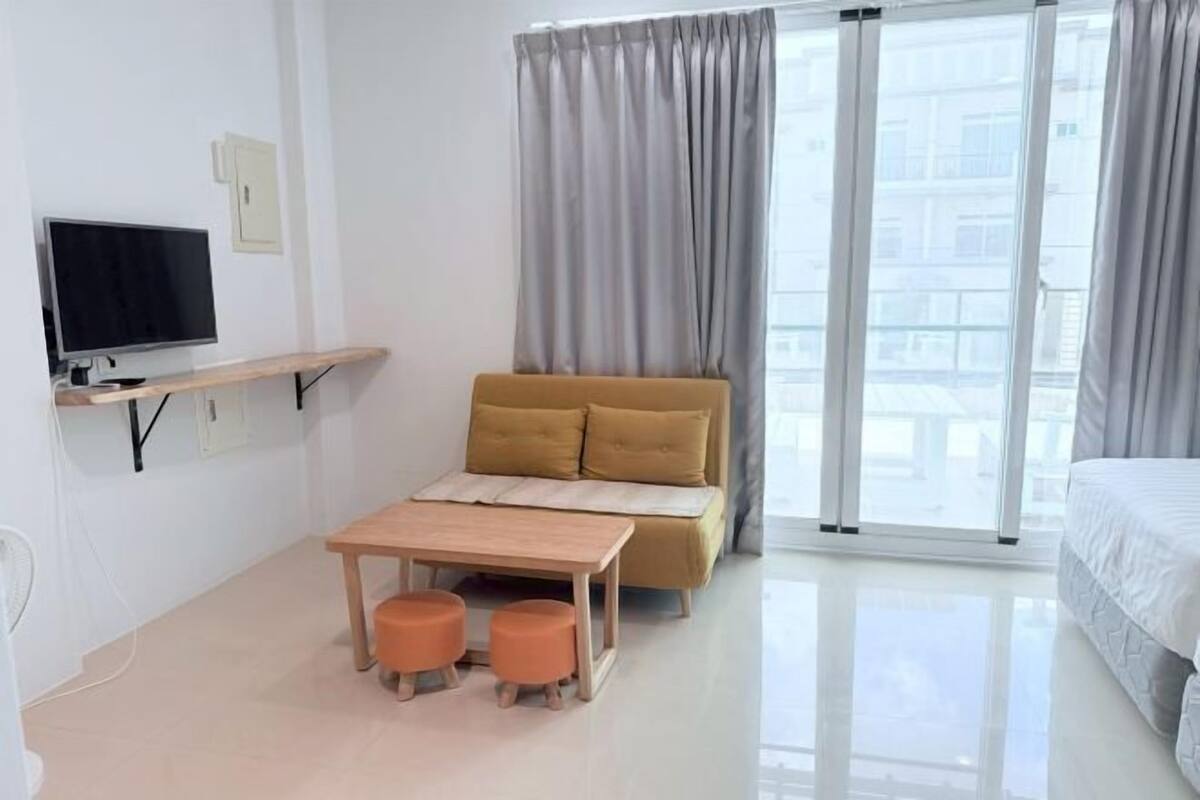 Una habitación de hotel moderna con sofá, una mesita, televisor y balcón con cortinas.