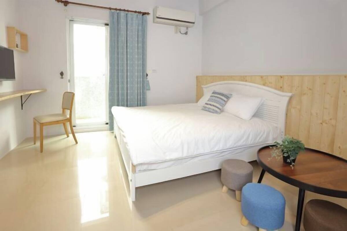 Un dormitorio con cama, una silla, una mesita con una planta y un equipo de aire acondicionado.