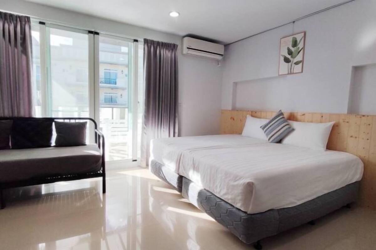 Habitación de hotel con cama, sofá, aire acondicionado y ventana con cortinas.