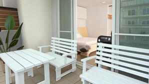 A balcony with white furniture, a sliding door leading to a bedroom, and a view of a building. - Xiaodou B&B (Taitung)